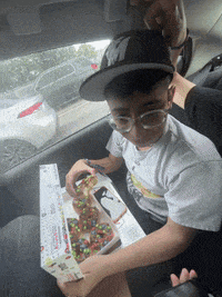 a boy wearing glasses and a hat is sitting in a car holding a box of donuts