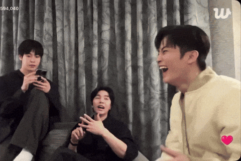 a group of young men are sitting on a couch and one of them is laughing with a w logo in the corner