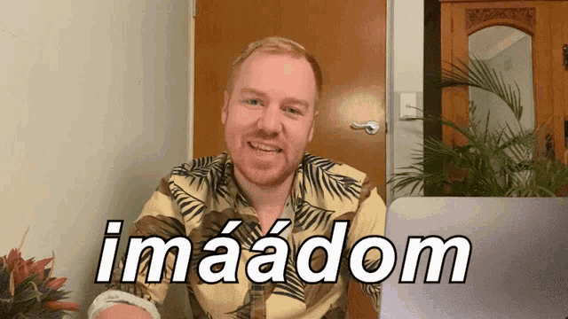a man in a hawaiian shirt is smiling in front of a laptop that says imaadom on it
