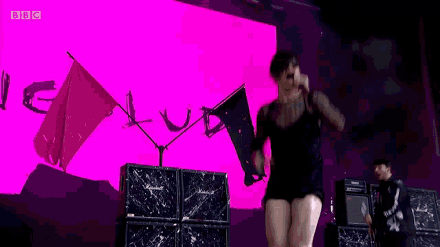 a woman singing into a microphone in front of a pink cube