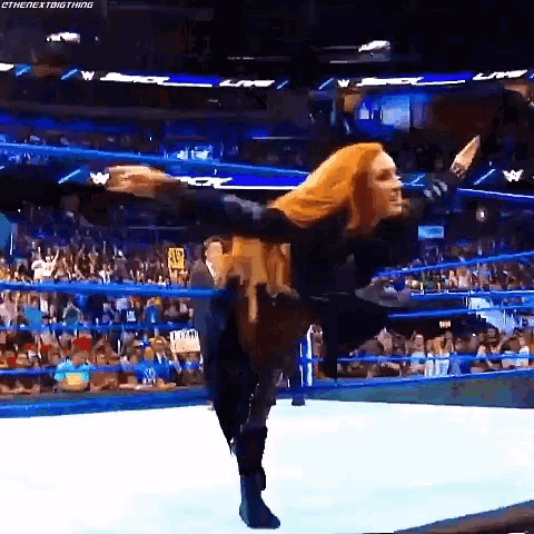 a woman is standing in a wrestling ring with her arms outstretched and a crowd watching .