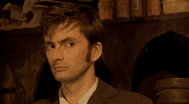 a man in a suit and tie is making a funny face while standing in a dark room .