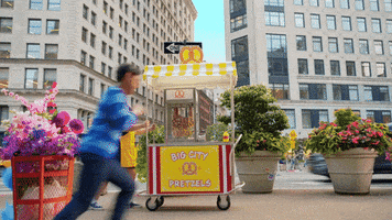 a man is running towards a big city pretzel cart