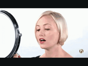 a woman looks at herself in a mirror with a green g on the bottom