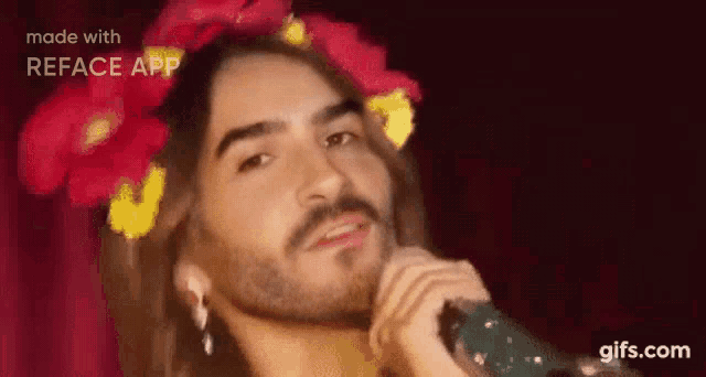 a man with long hair and a beard is singing into a microphone with flowers in his hair .