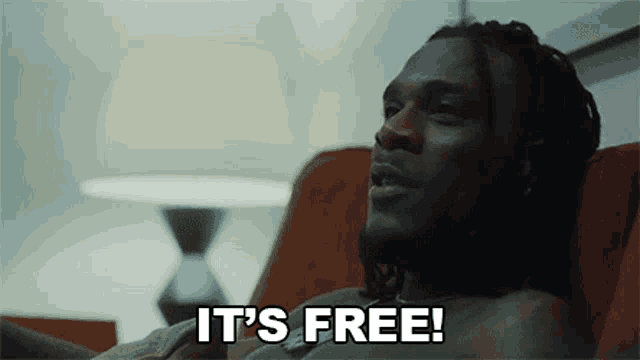 a shirtless man is sitting on a couch with the words `` it 's free '' written on his face .
