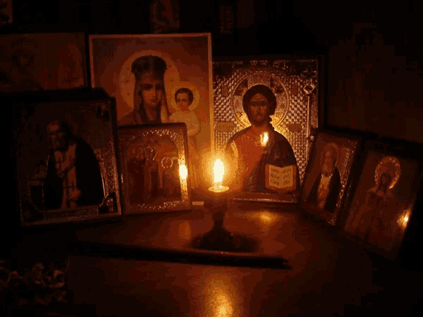 a candle is lit in front of several religious icons including one of jesus holding a book