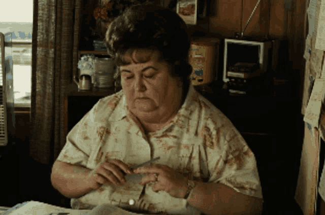 a woman is sitting at a table with a box of pringles on the wall behind her