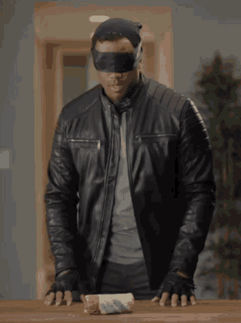 a blindfolded man in a black leather jacket holds a roll of bread