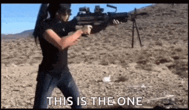 a woman is holding a rifle in a desert and saying `` this is the one '' .