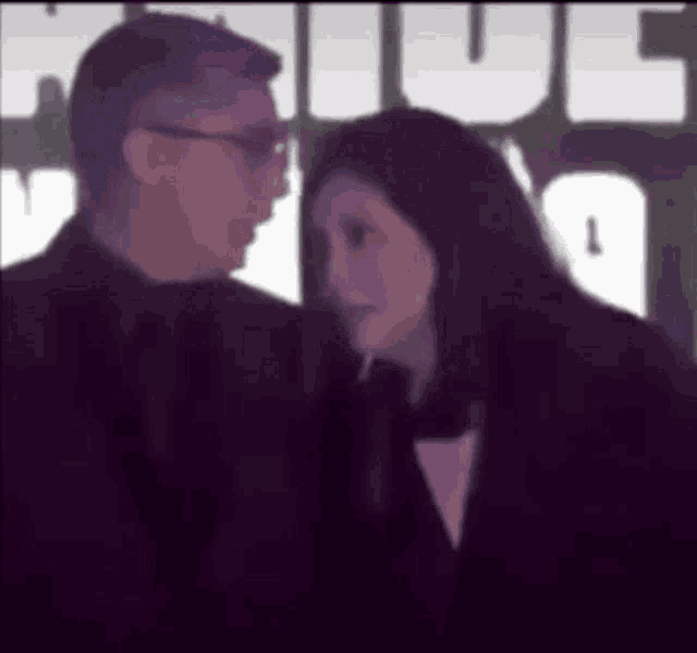 a man and a woman are standing next to each other and looking at each other in front of a sign .