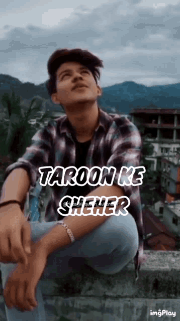 a young man in a plaid shirt is sitting on a ledge with the words taroon ke sheher written above him