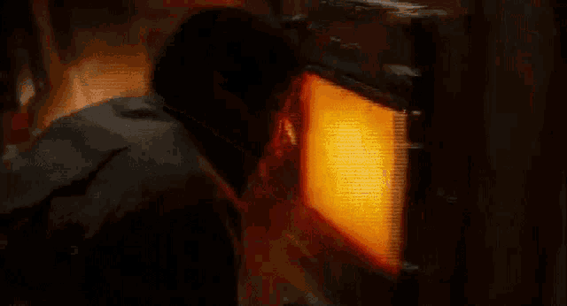a man is looking into a microwave oven with a bright orange light coming out of it .