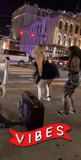 two women are dancing on a street with a red banner that says vibes on it