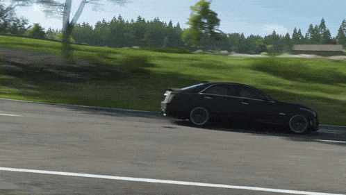 a black car is driving down a road near a grassy hillside