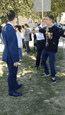 a man in a suit and a man in a black shirt are standing in a grassy field