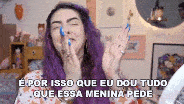 a woman with purple hair and blue nails is making a funny face with her hands in the air .