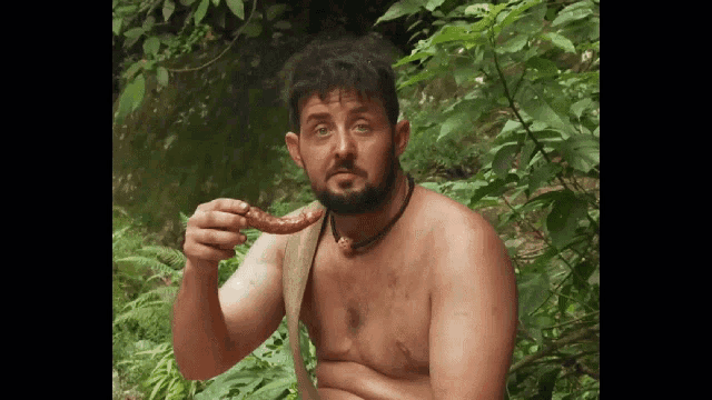 a shirtless man with a beard is eating a piece of meat