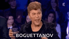 a man is sitting in front of a crowd holding a glass of wine and saying boguettenov .