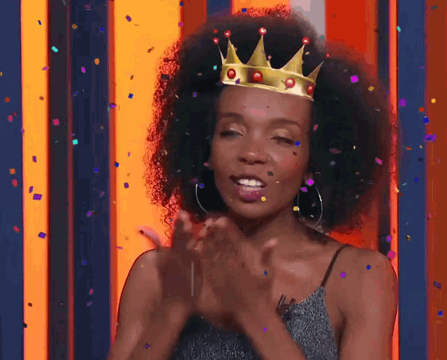 a woman wearing a crown applauds with confetti falling around her