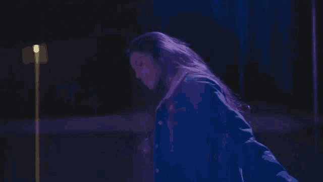 a woman in a denim jacket is standing in front of a blue light