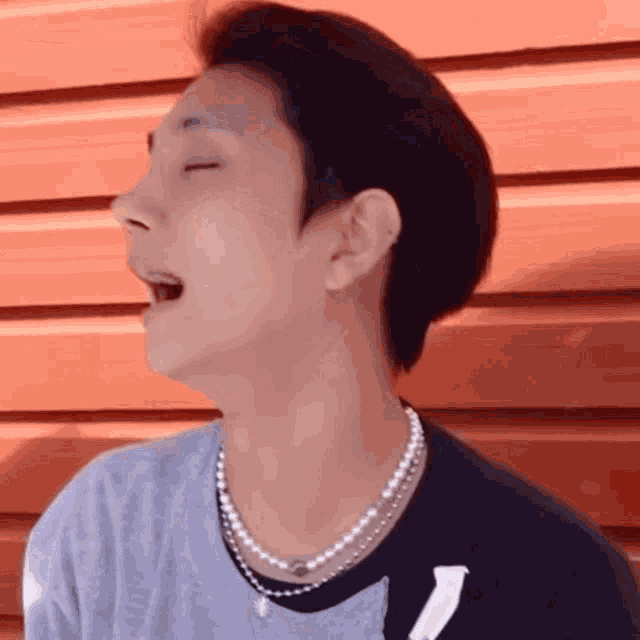 a man wearing a pearl necklace is laughing with his mouth open .