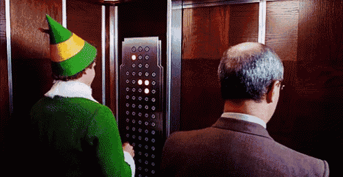 a man in a suit and an elf in a green hat are in an elevator .