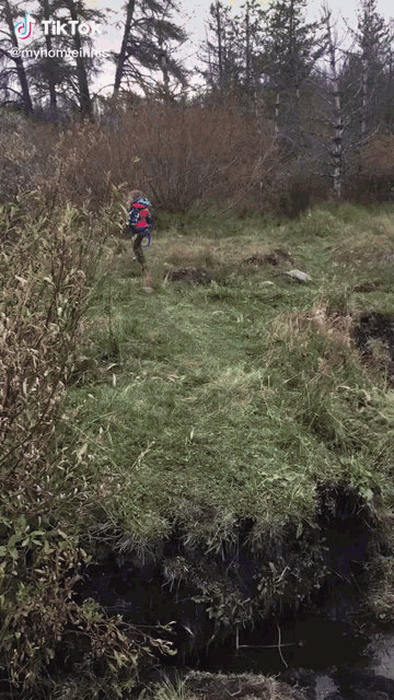 a boy in a red jacket is running through a grassy field