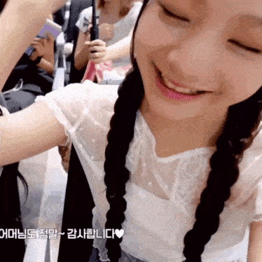 a girl with braids and a white shirt smiles for the camera with a heart in the corner