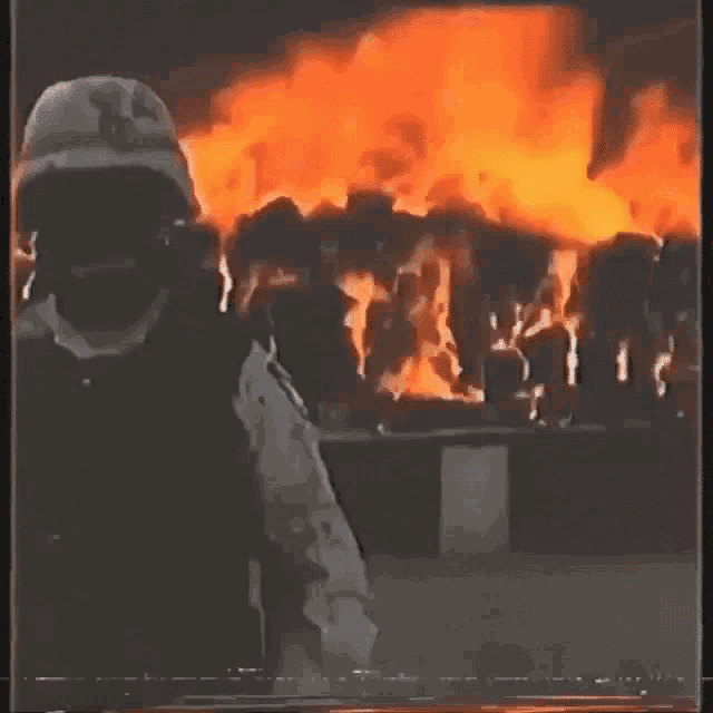 a man in a helmet stands in front of a large fire .