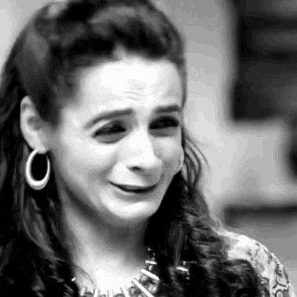 a woman is crying in a black and white photo while wearing hoop earrings and a necklace .