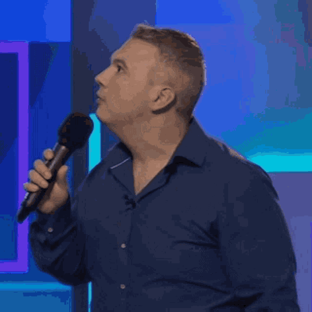 a man in a blue shirt is holding a microphone in his hand