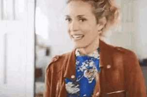 a woman in a brown jacket and a blue floral shirt is smiling .