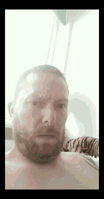 a man with a beard is making a funny face while sitting in front of a window .