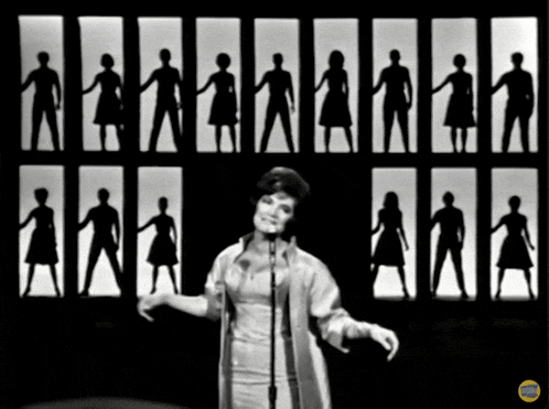 a woman is singing into a microphone in front of a wall of paper people