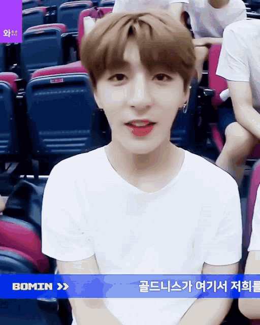 a boy in a white t-shirt is sitting in a row of seats with the word bomin on the screen