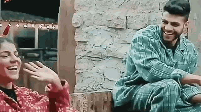 a man and a woman are sitting next to each other in front of a brick wall and laughing .