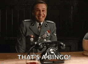 a man in a military uniform is sitting at a table talking on a telephone and smiling .