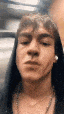 a young man wearing a hoodie and a necklace is making a face .