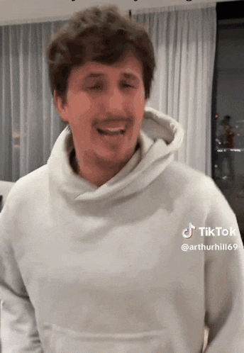 a man in a white hoodie is making a funny face while standing in front of a window .