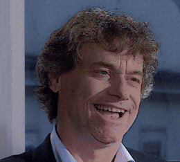 a man with curly hair wearing a suit and a white shirt is smiling