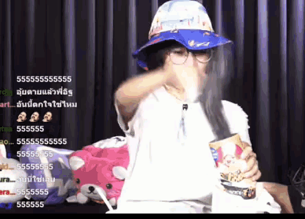 a woman wearing a blue hat and glasses is eating a can of popcorn