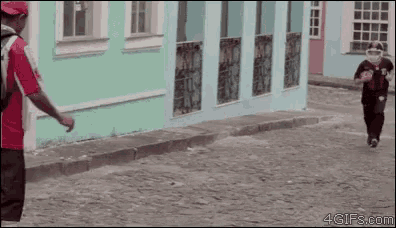 a man in a red shirt is walking down a cobblestone street next to a green building .