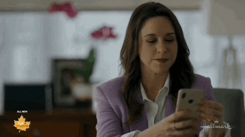 a woman in a purple jacket is looking at a cell phone with a hallmark logo on the bottom