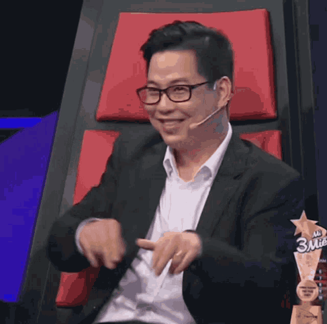 a man wearing glasses and a suit is sitting in a chair with a 3rd place trophy in front of him