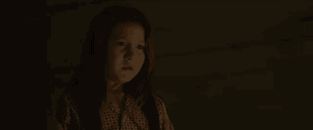a little girl with long red hair is standing in the dark