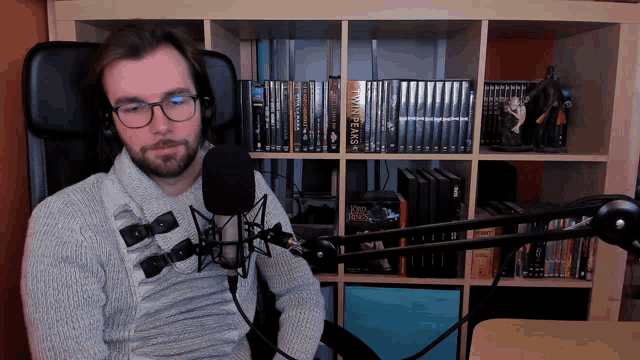 a man sitting in front of a microphone with a bookshelf behind him that has the word twin peaks on it