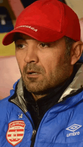 a man wearing a red hat and a blue jacket with umbro on the sleeve