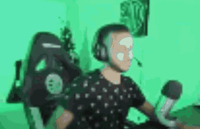 a man wearing headphones and a face mask is sitting in front of a green screen .