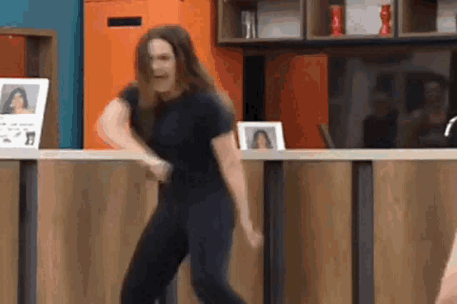 a woman in a black shirt and black pants is dancing in front of a wooden counter .
